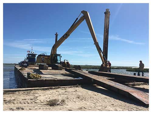 Long-reach excavator working on a barge at the water's edge