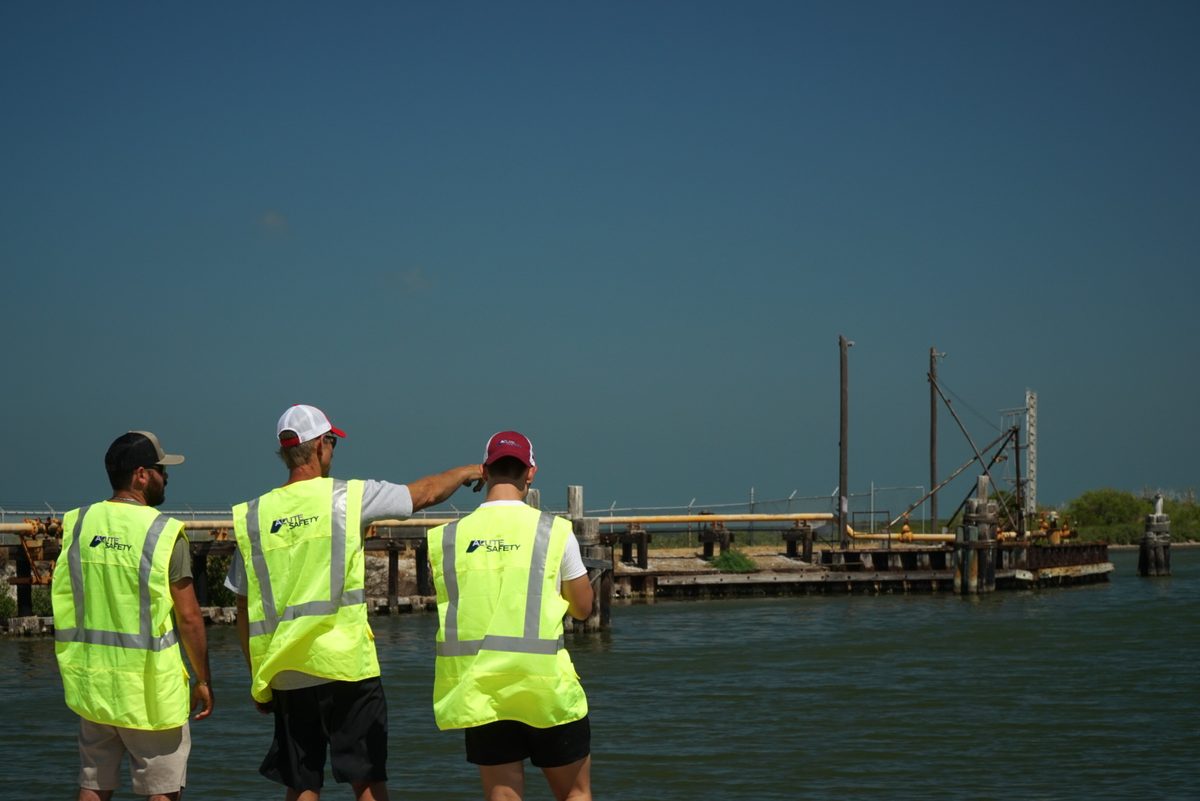 Three Acute Safety reps in branded hi-vis vests looking over a waterfront terminal site in Rockport, Texas